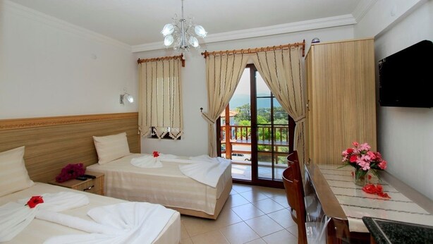 A hotel room with two beds, a dining table with chairs, a chandelier, and a balcony with curtains. - Deger Apart (Ula)