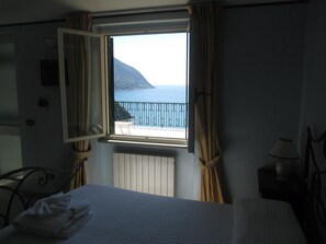 A hotel room with a bed, a window with curtains, a view of the sea, and a chair outside. - Hotel Leopold (Moneglia)
