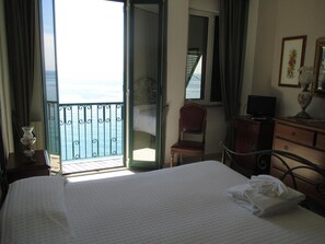 A hotel room with a bed, a chair, a dresser, a television, and a view of the sea through an open door. - Hotel Leopold (Moneglia)