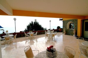 An outdoor patio with white wicker furniture and a view of the sea. - Hotel Leopold (Moneglia)