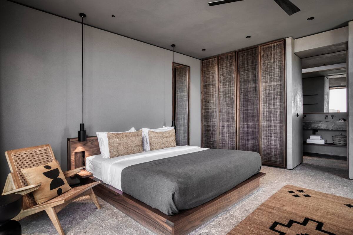 A modern bedroom with a large bed, a wooden chair, a bedside table, and a wardrobe.