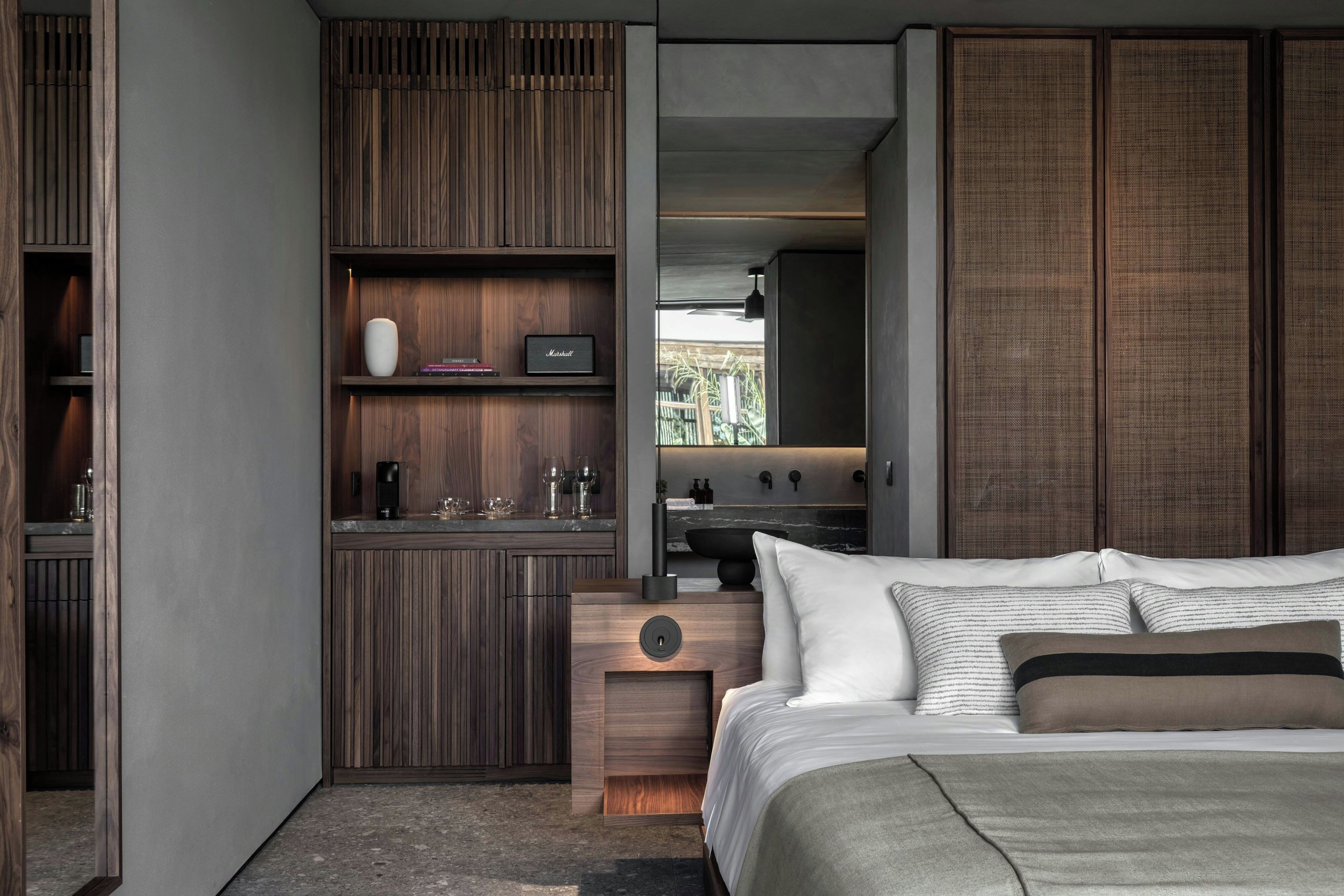 A modern bedroom with a bed, a wooden wardrobe, and a small kitchenette area.