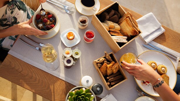 A wooden table with various breakfast items including toast, pastries, and a bowl of fruit.
