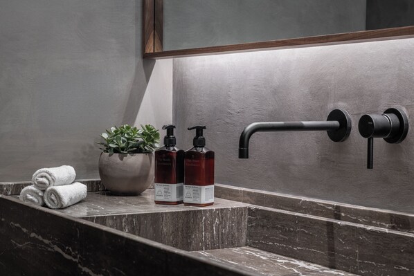A bathroom with a marble sink, two hand soap bottles, a potted plant, and a towel. - Domes Zeen Chania, a Luxury Collection Resort, Crete (Chania)