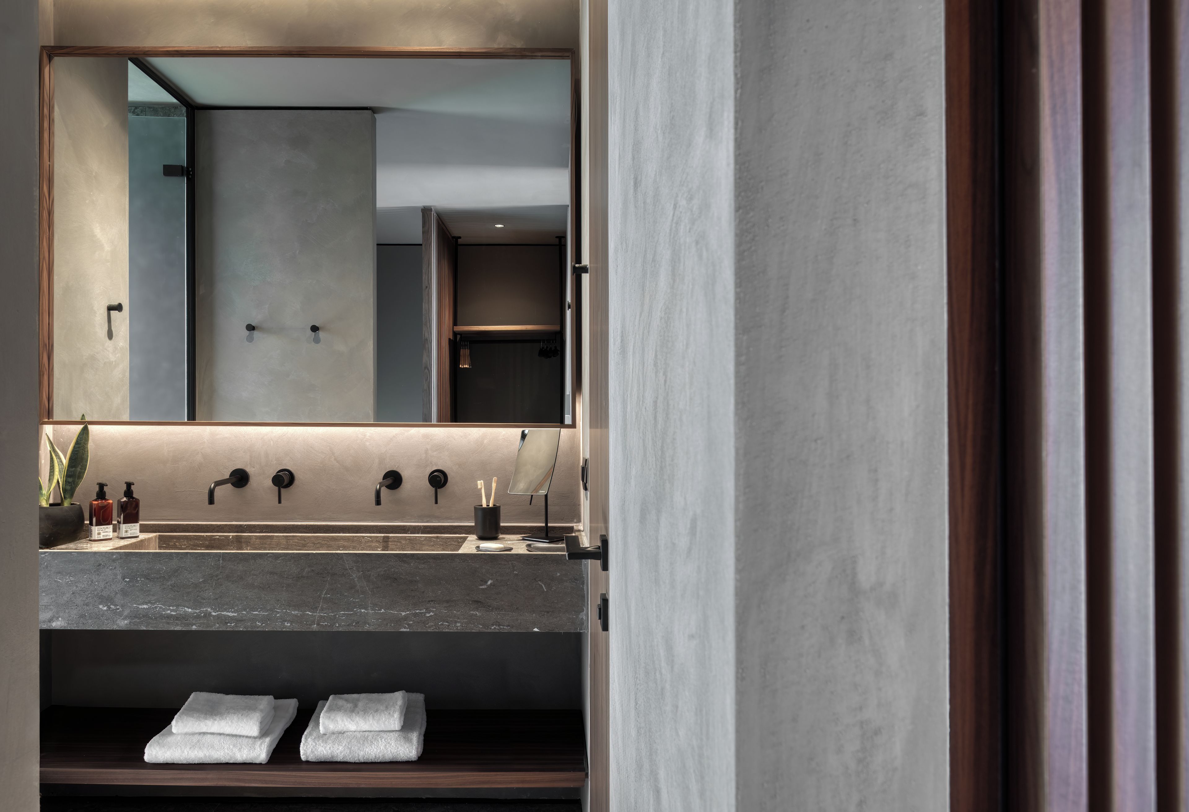 A modern bathroom with a large mirror, a sink with three faucets, and a towel rack with folded towels.