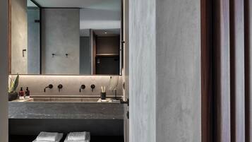 Un baño moderno con un espejo grande, un lavabo con tres grifos y un perchero con toallas dobladas.