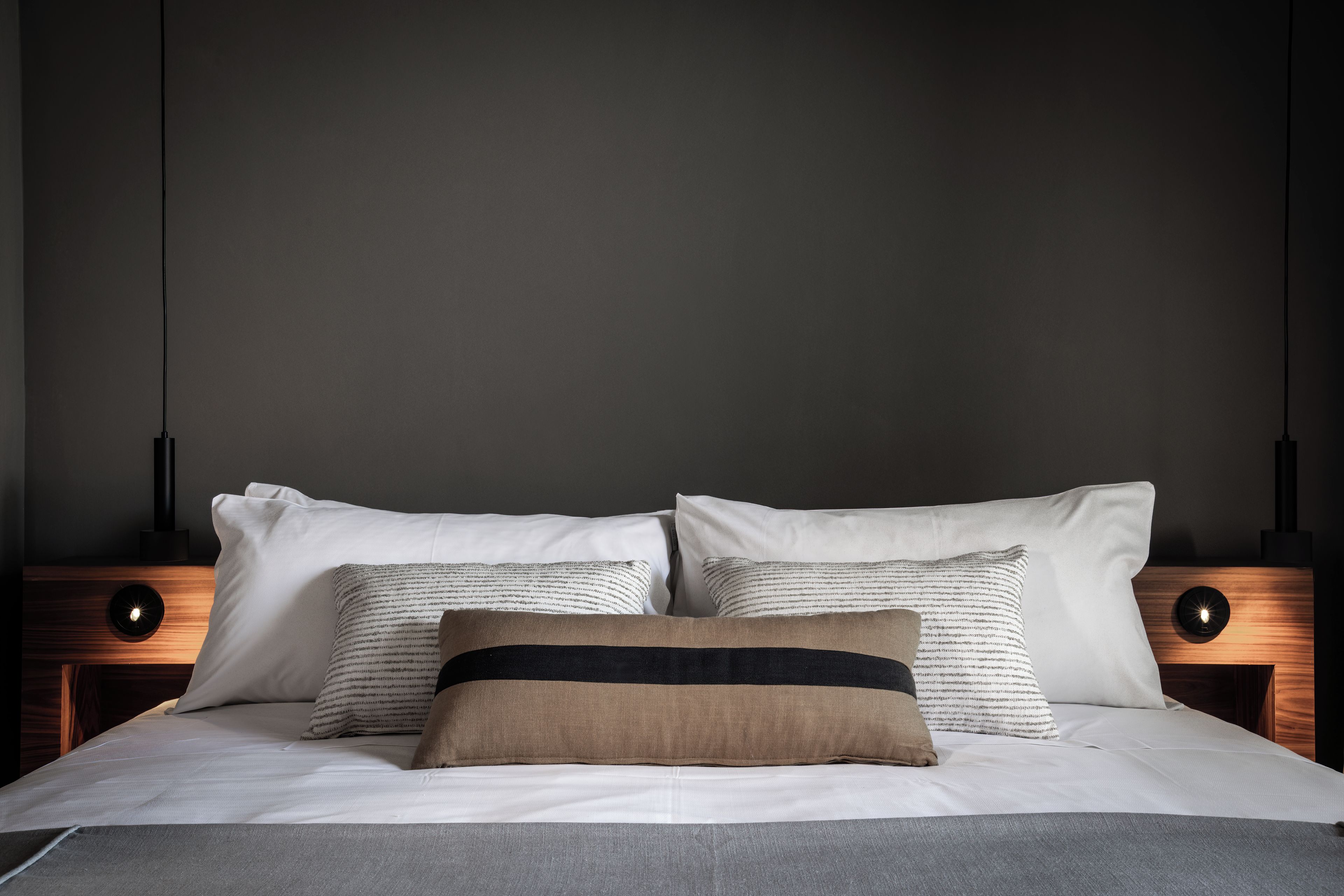 A neatly made bed with white and striped pillows, a brown accent pillow, and a grey blanket.