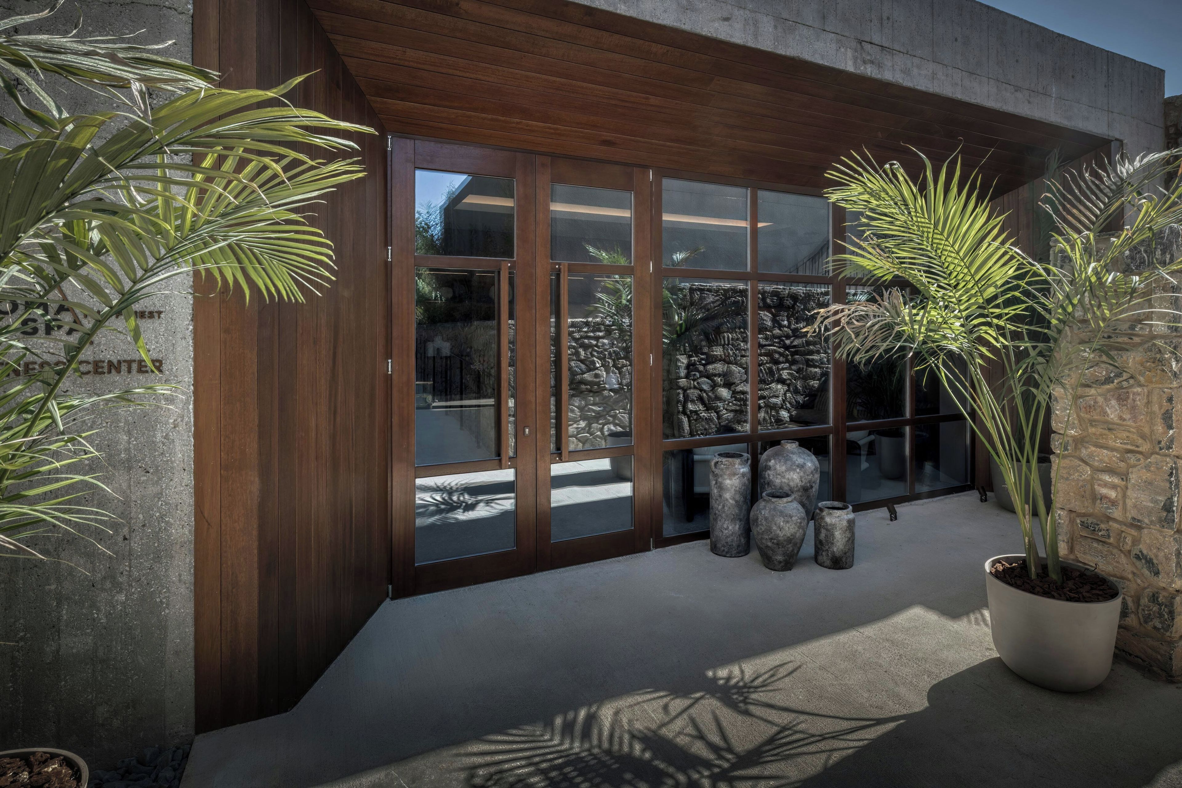 A building entrance with a wooden facade, large glass doors, and potted plants.