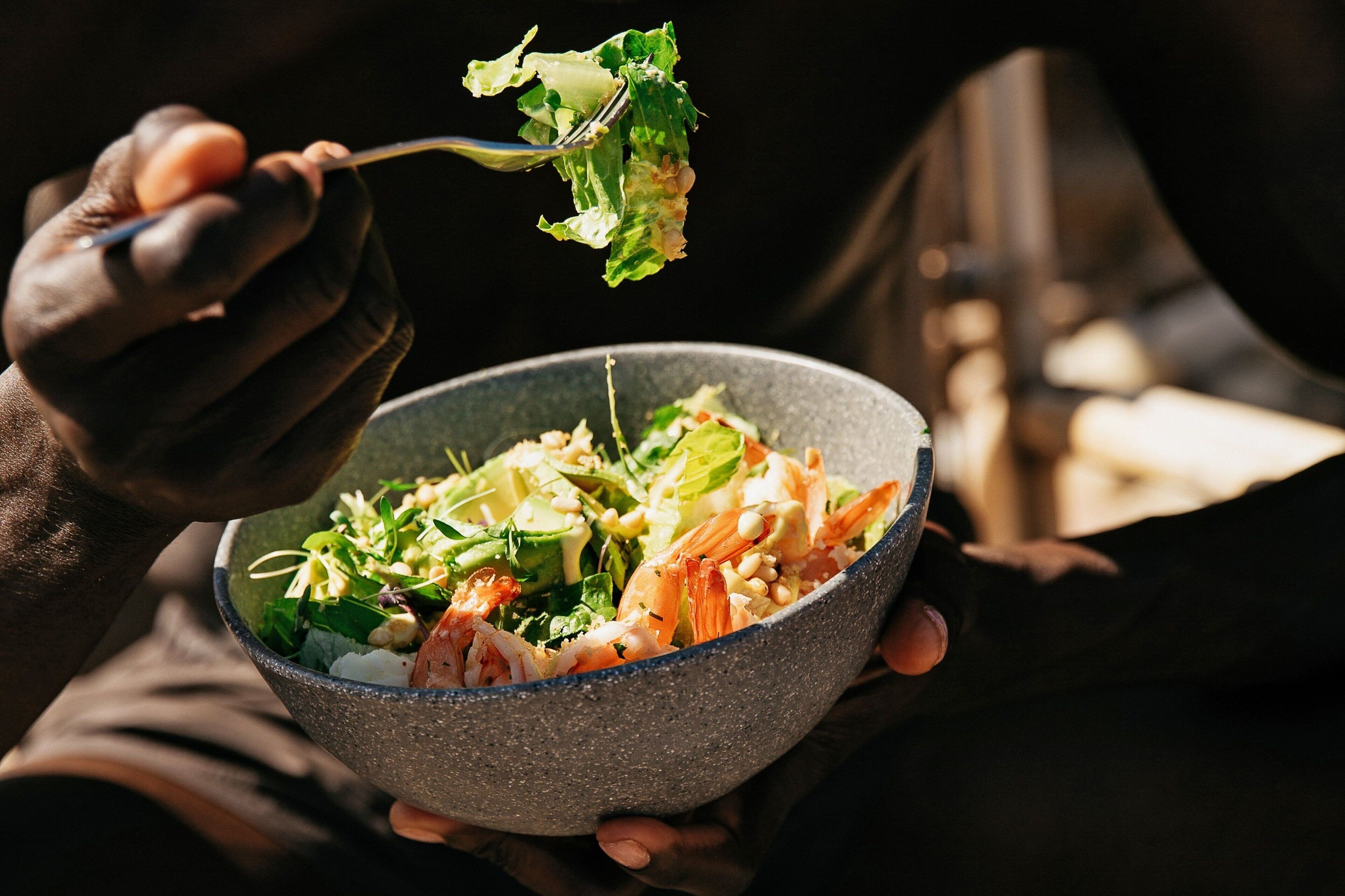 A person holding a bowl of salad with a fork.