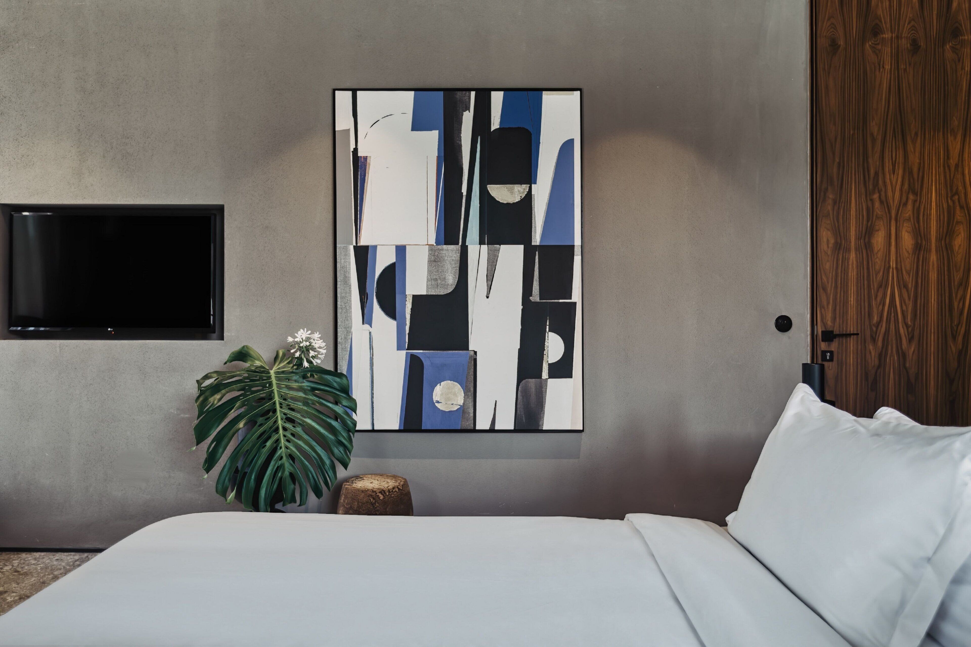 A modern bedroom with a large abstract painting, a television, a wooden door, and a plant.