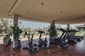 A covered outdoor gym area with exercise equipment, potted plants, and a view of the surrounding landscape.