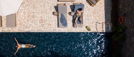 An aerial view of a swimming pool area with lounge chairs, a sunbed, and a person swimming.