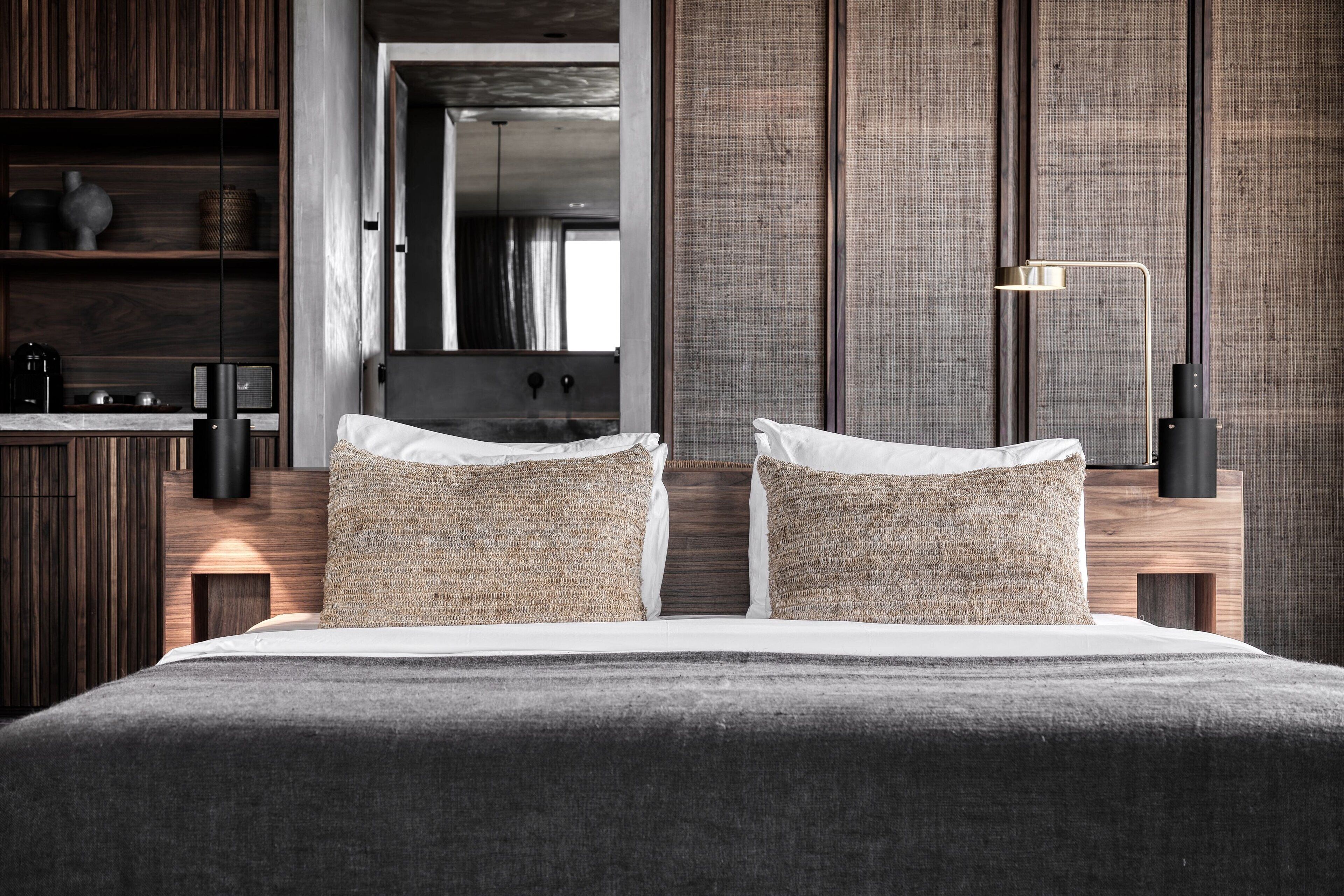A modern bedroom with a large bed, wooden headboard, and a bedside table with a lamp.