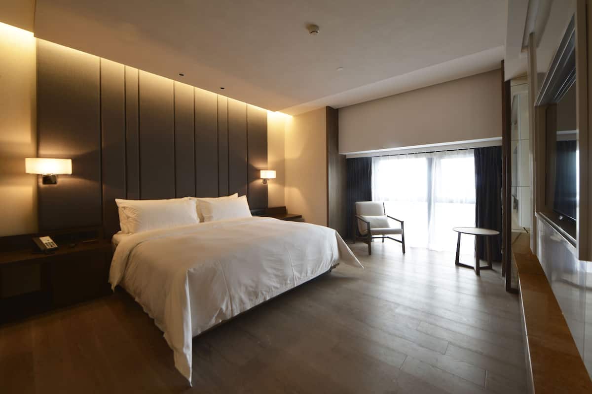 Habitación de hotel con una cama grande, mesitas de noche, una silla, una pequeña mesa y un televisor.