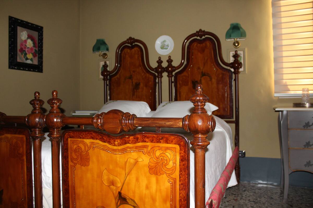Una cama de madera con cabecera y piecera ornamentados, una mesita de noche con una lámpara y un cuadro enmarcado en la pared.