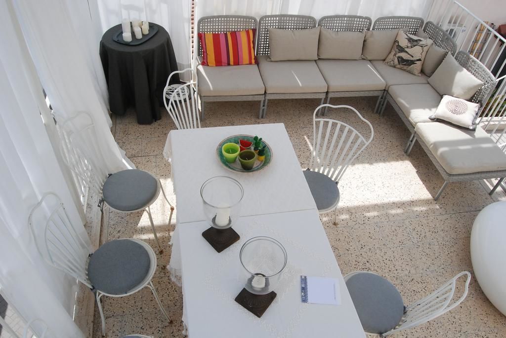 A sunlit outdoor seating area with a white table, chairs, and a sofa.