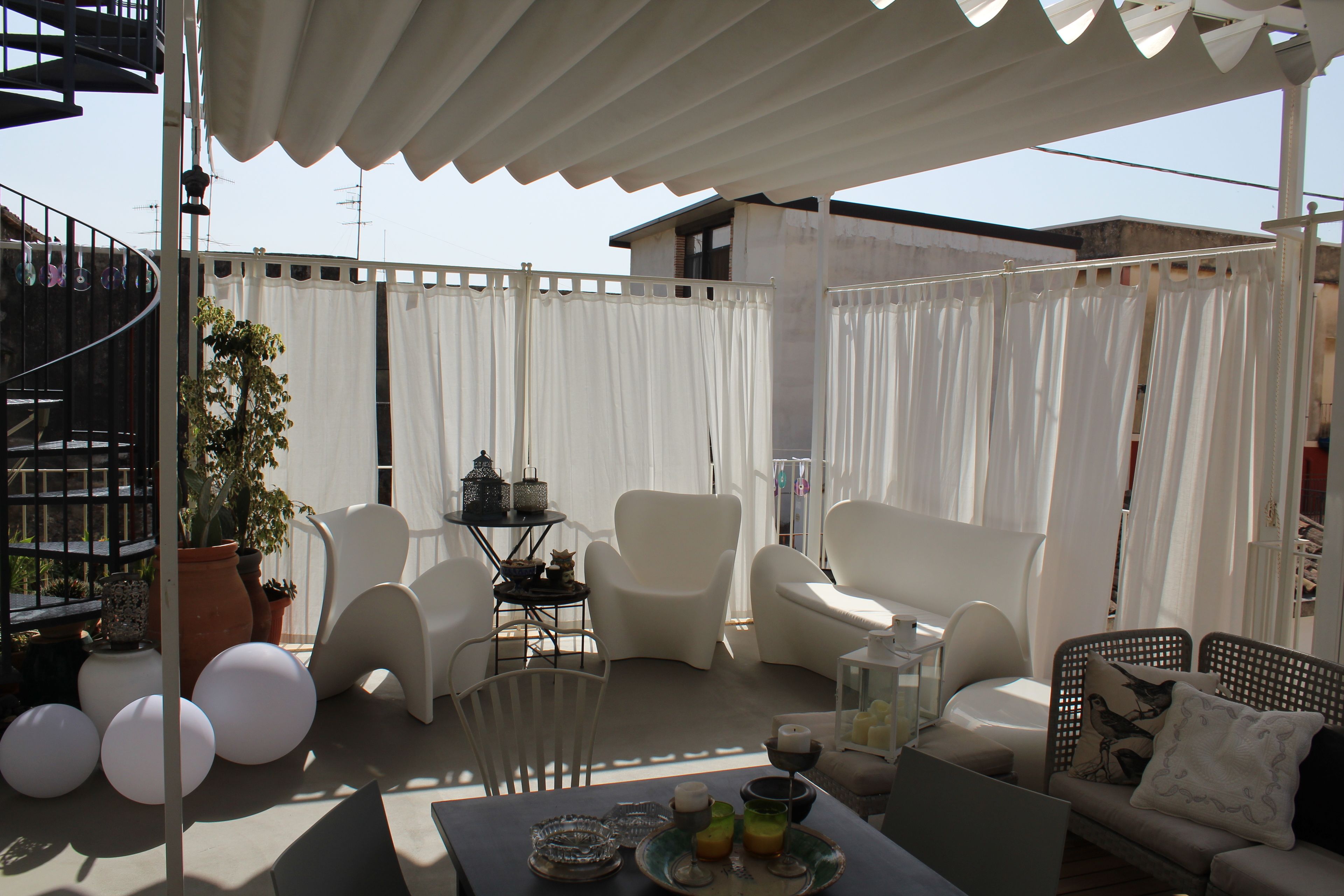 Un espace extérieur abrité avec des chaises blanches, une table avec des boissons et une plante en pot.