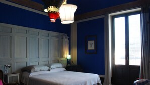 A hotel room with a large bed, a nightstand, a chair, and a window with curtains. - Kemmare (Riposto)