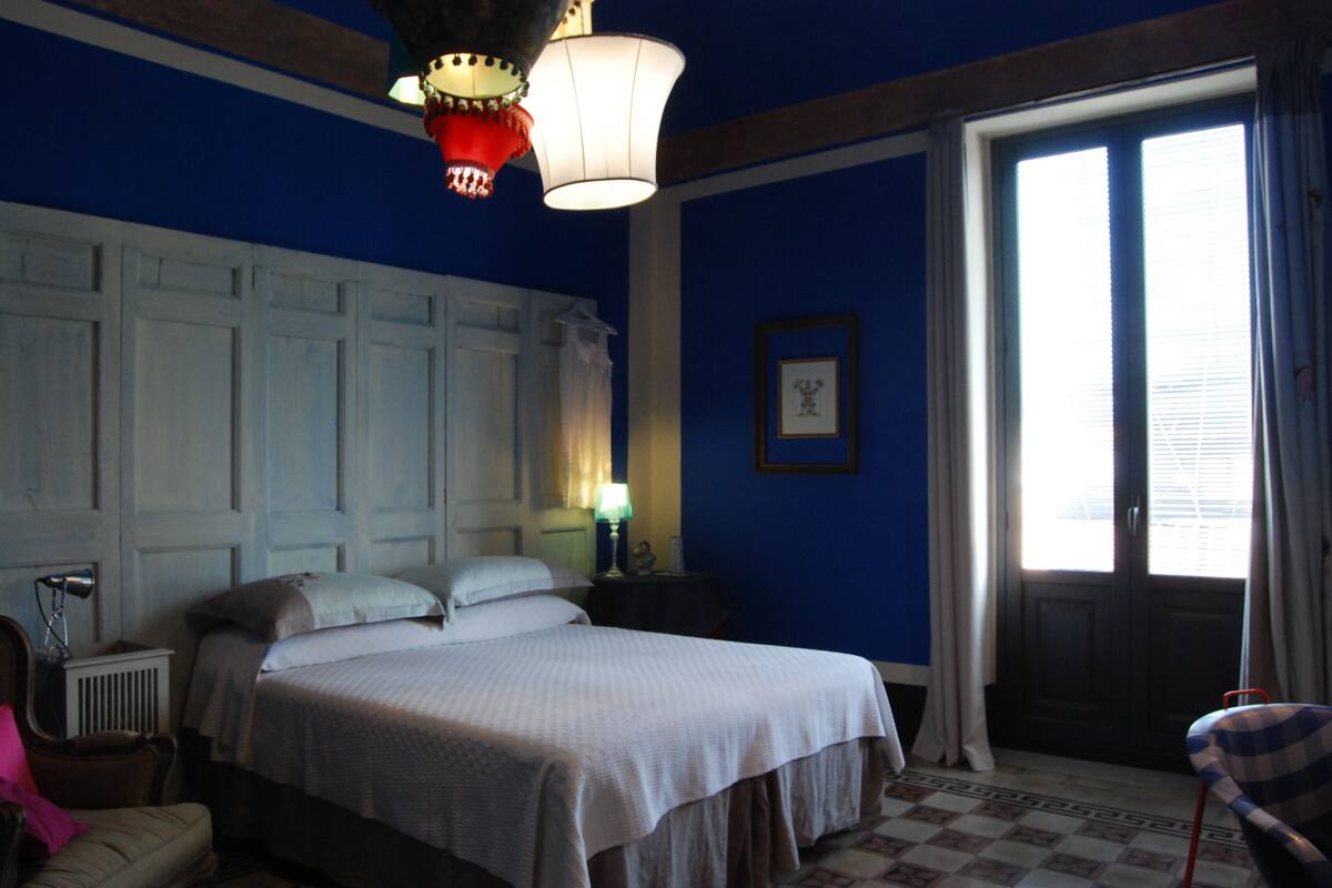 Habitación de hotel con una cama grande, una mesita de noche, una silla y una ventana con cortinas.