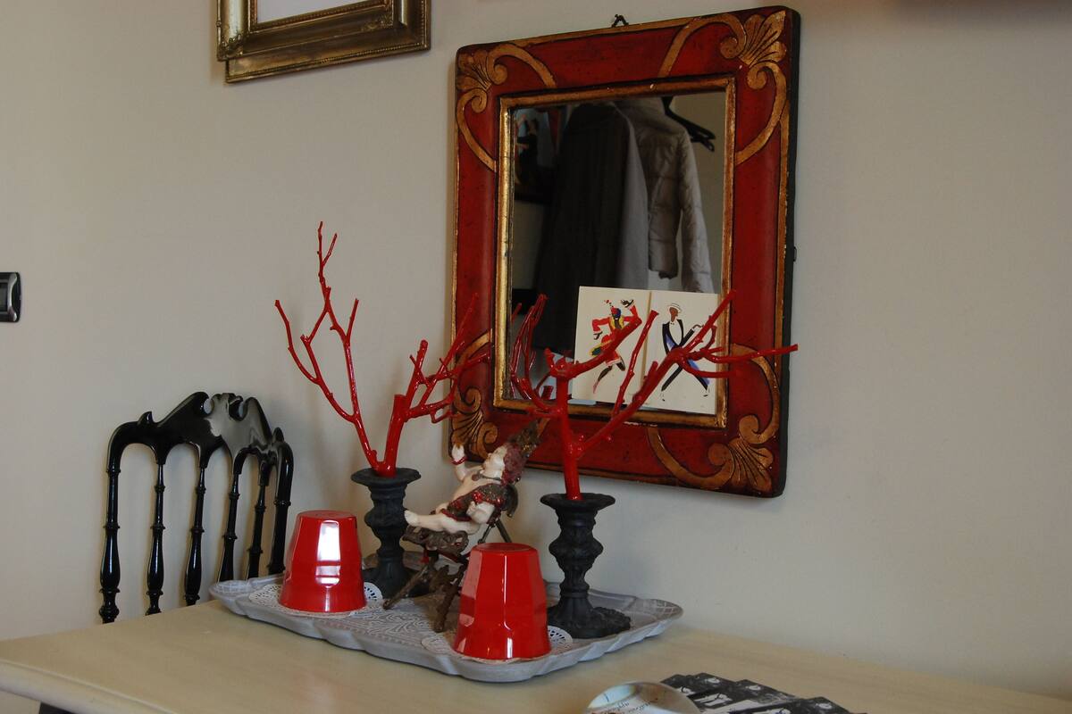 Una habitación con un espejo, una bandeja decorativa con objetos rojos y una silla de diseño único.