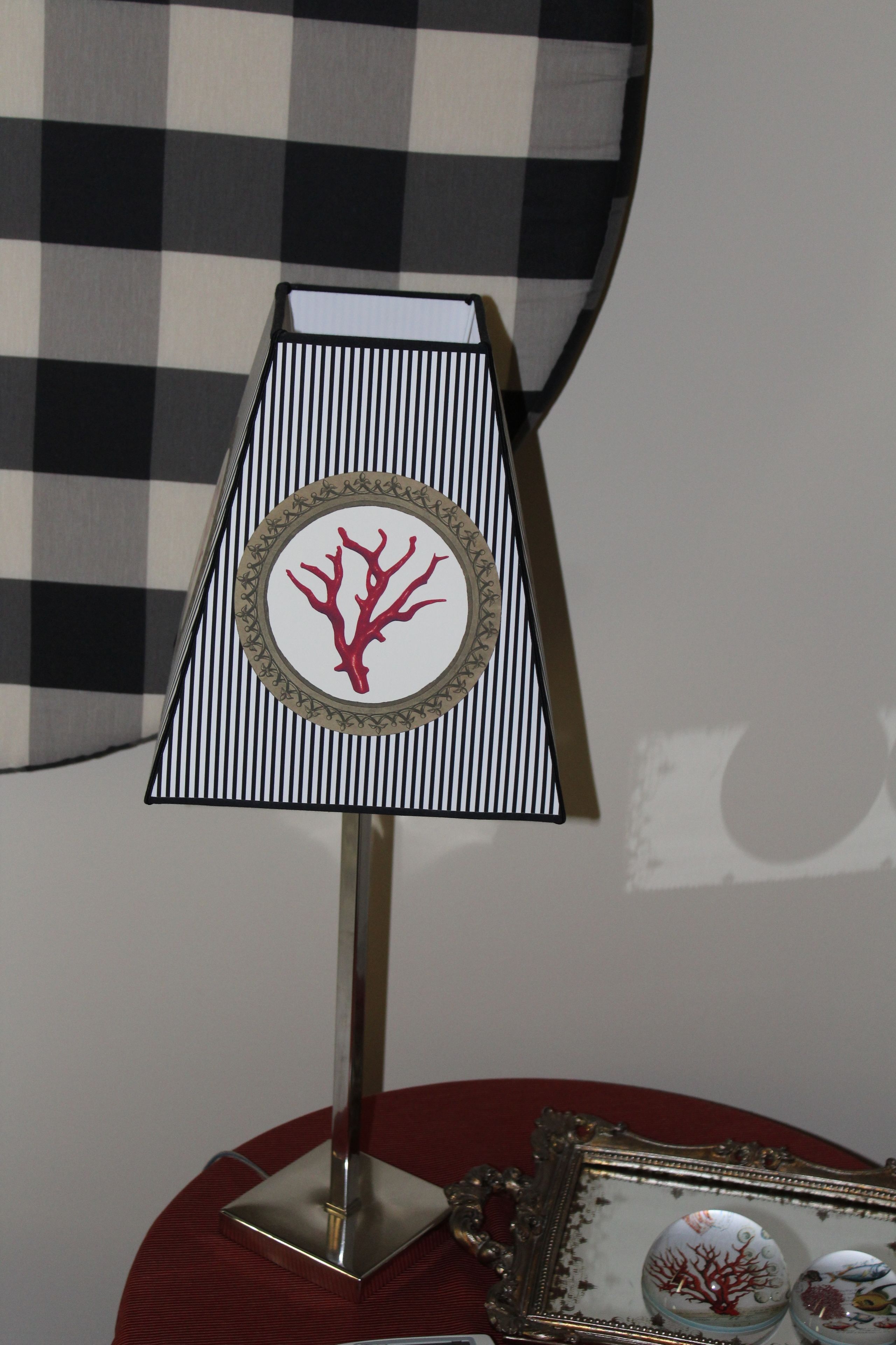 Une lampe dotée d’un abat-jour à rayures et d’un pied décoratif, posée sur une table ronde recouverte d’une nappe rouge.