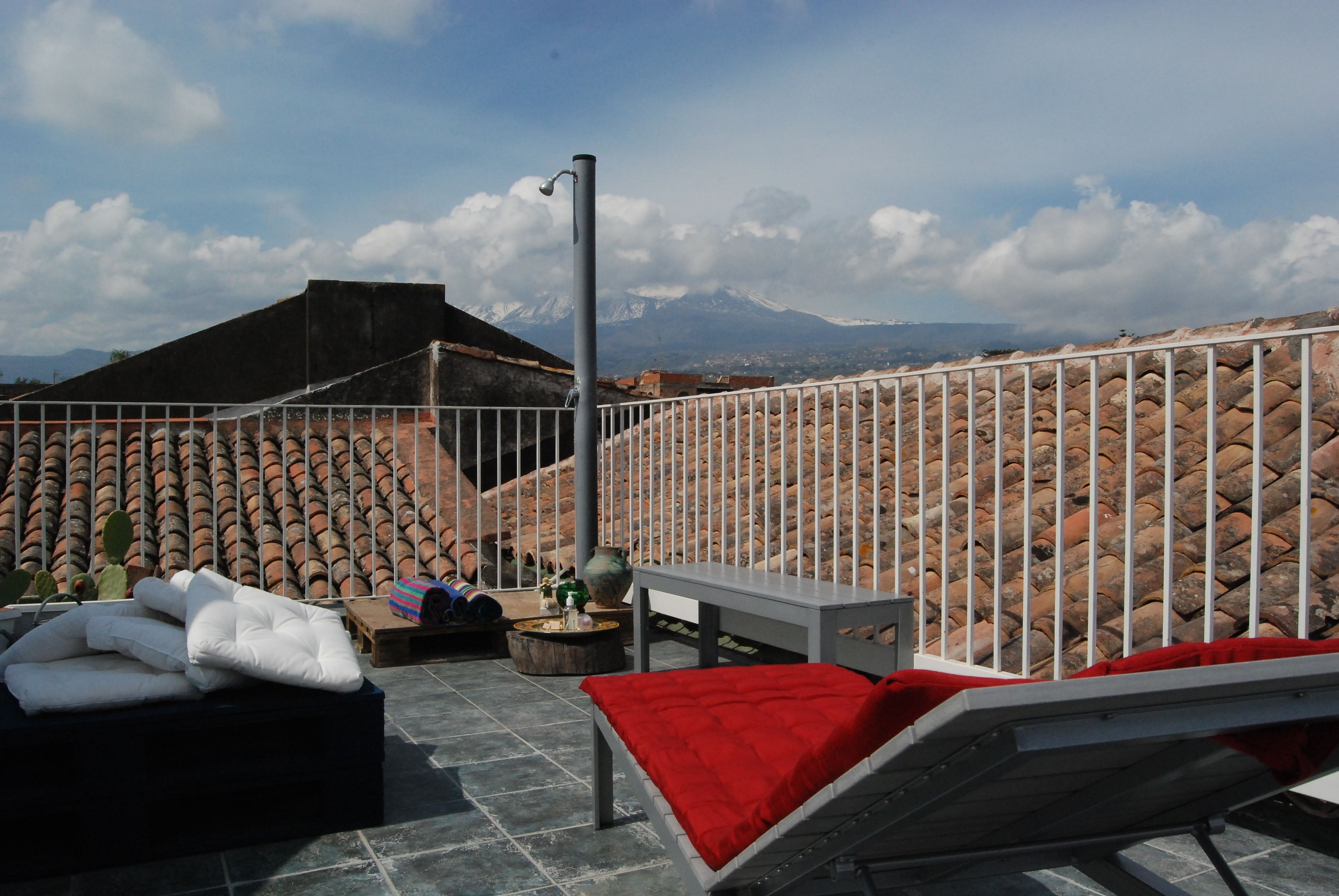 Une terrasse sur le toit offrant une vue sur une chaîne de montagnes, avec une rambarde en métal et un espace détente comprenant des coussins et une table.