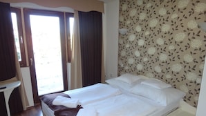 A hotel room with a bed, a small table, and a window with curtains. - Hotel Viktória Vendégház (Balatonalmadi)