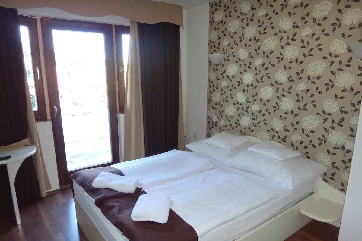 A hotel room with a bed, a small table, and a window with curtains.