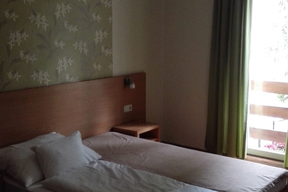 A hotel room with a bed, a nightstand, a headboard, a window with curtains, and a hanging light fixture.