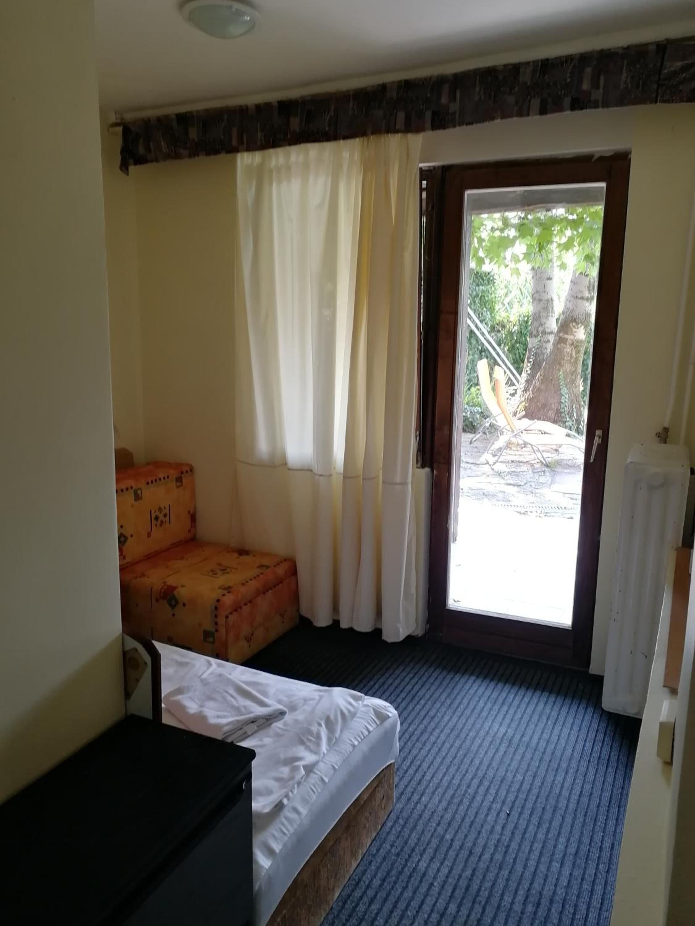 A small, simple room with a bed, a small table, and a window with curtains.
