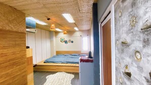 Un dormitorio con piso de madera, cama con ropa de cama azul, alfombra blanca y pared decorada con motivos náuticos.