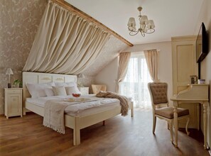A bedroom with a large bed, a nightstand, a chair, a desk, and a television. - Barackvirág Apartmanház (Tihany)