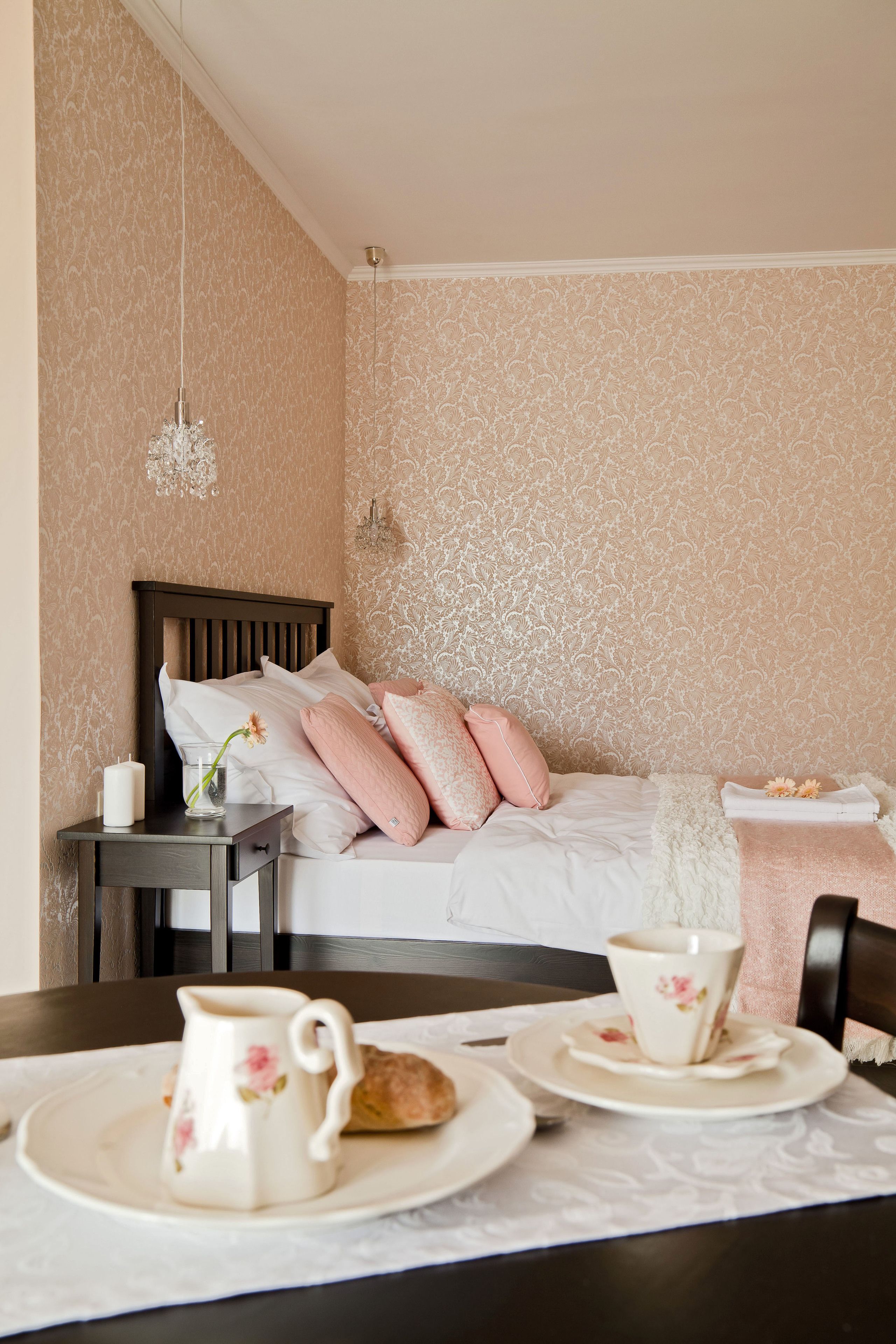 A neatly arranged bedroom with a bed, bedside table, and a dining table with plates and a pitcher.