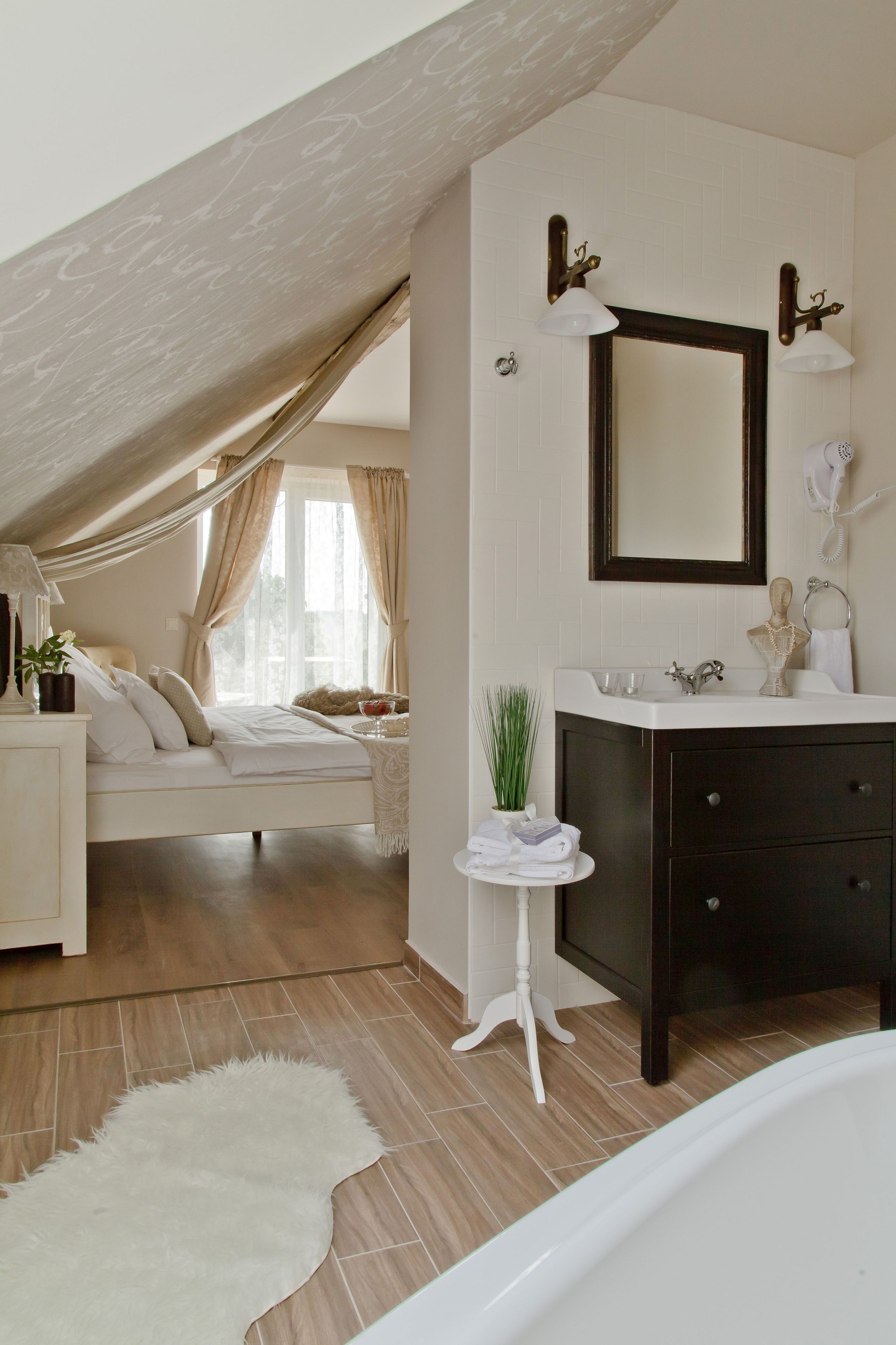 A bedroom with a sloped ceiling, a bed, a bedside table with a lamp, and a window with curtains.
