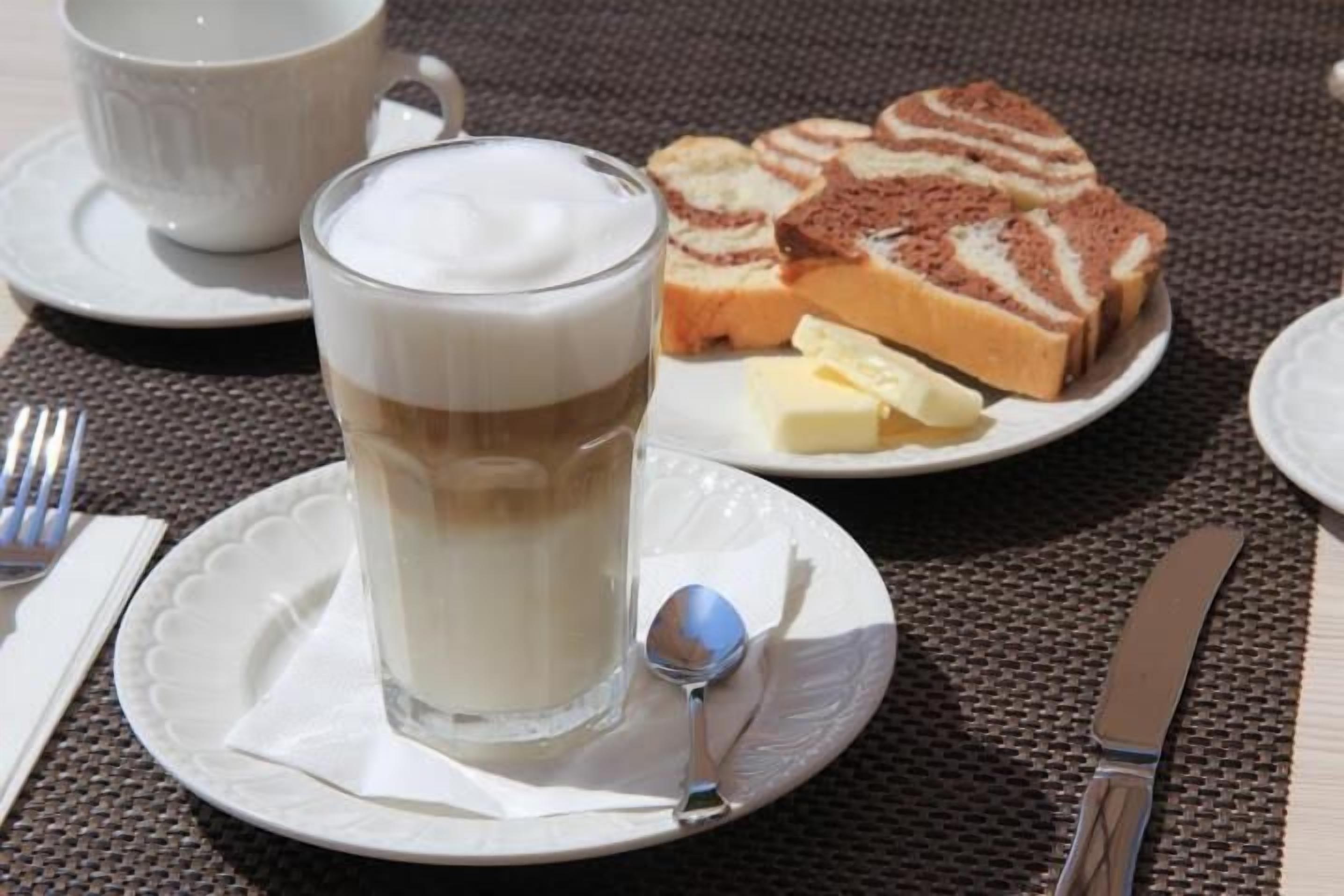 A breakfast setting with a glass of milk, a cup of coffee, a plate of bread, and a butter knife.