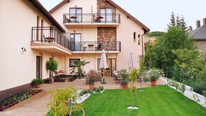 Una casa de dos pisos con balcón, mobiliario exterior y un jardín bien cuidado.