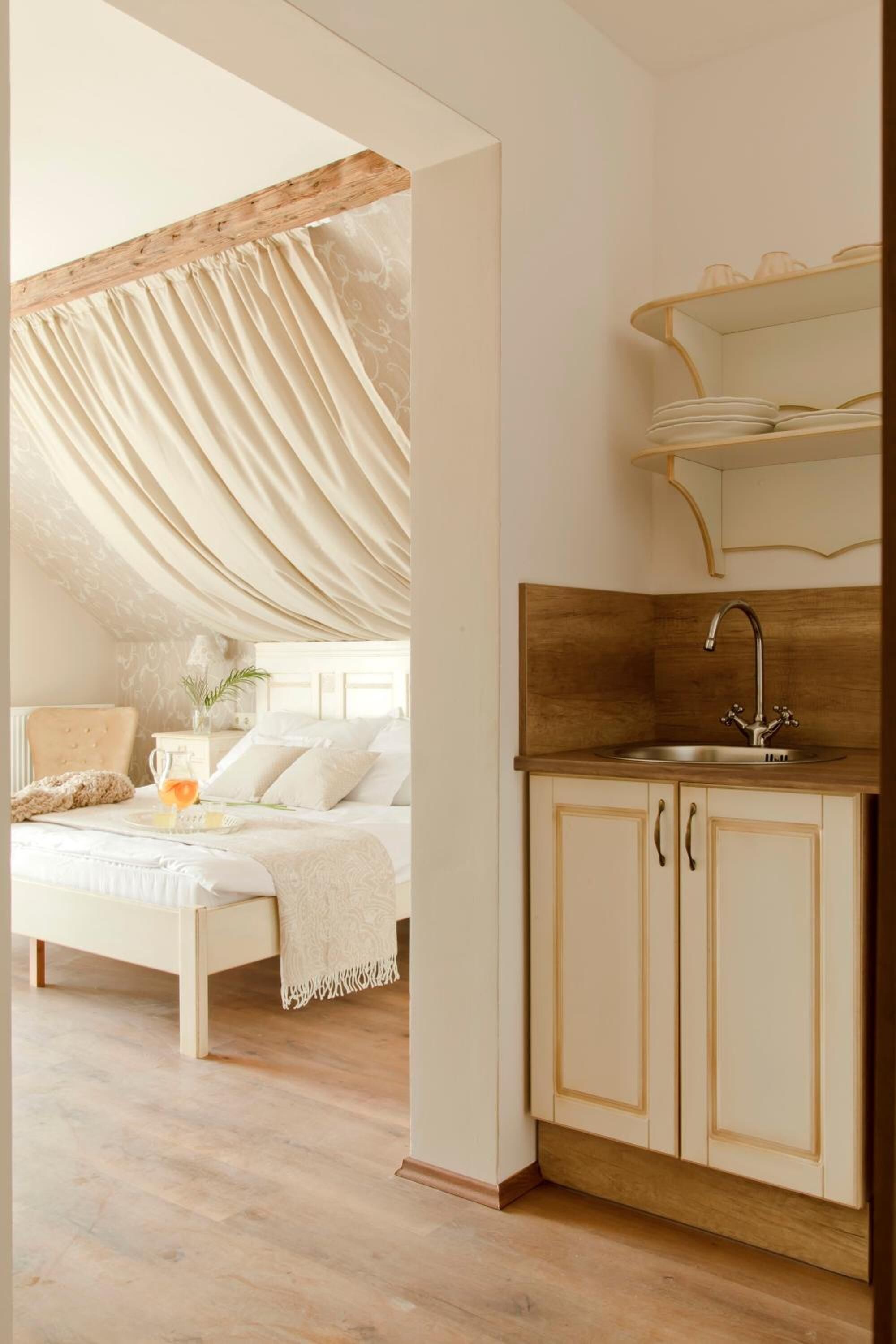 Un dormitorio con cama, una mesita de noche y una mesilla auxiliar. Hay una ventana con cortinas.