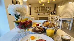 Desayuno con huevos, jamón, cruasanes y fruta sobre una mesa.