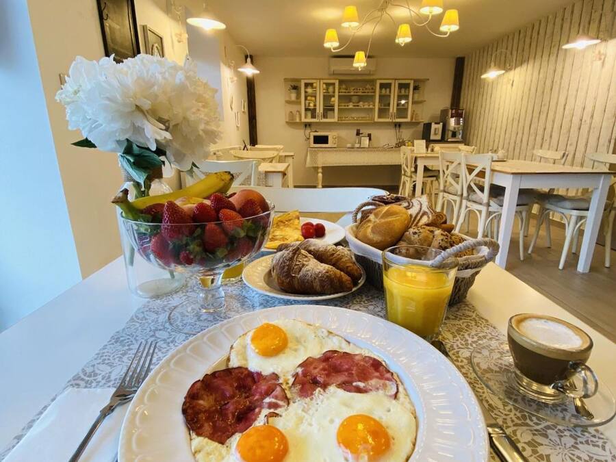 A breakfast setting with eggs, ham, croissants, and fruit on a table.