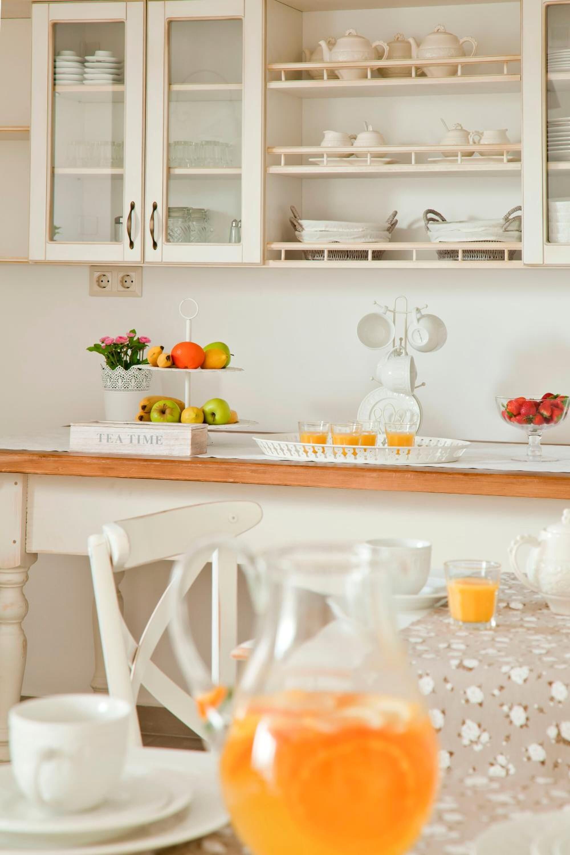 A kitchen with white cabinets, a tea set, and a fruit display.