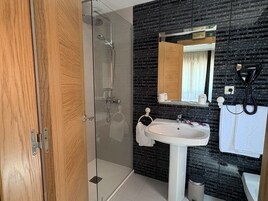 Un baño moderno con cabina de ducha de vidrio, un lavamanos blanco y un salpicadero de mármol negro.