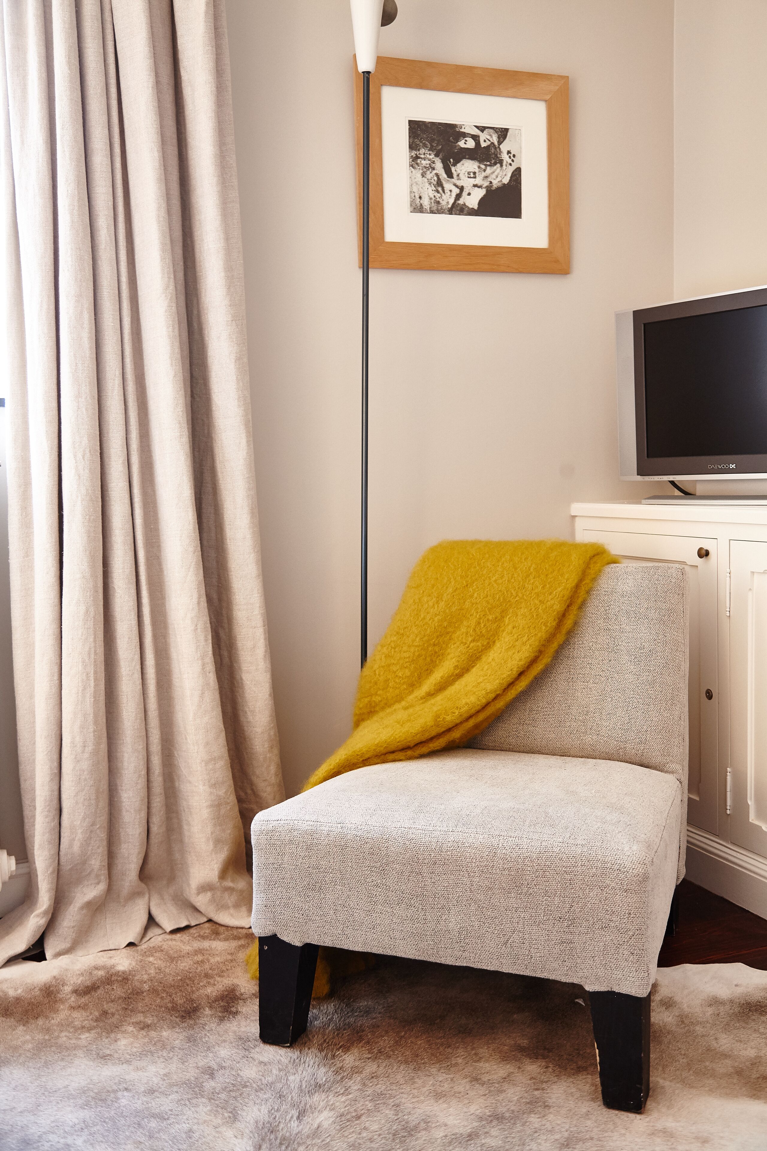 A chair with a yellow throw blanket, a television on a stand, and a framed picture on the wall.