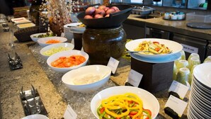 Un bufé con diversos platos, incluyendo verduras cortadas, pasta y una olla de papas.