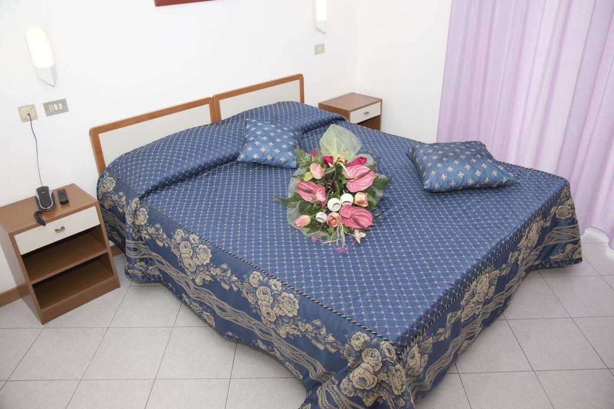 A neatly made bed with a floral arrangement, a bedside table with a lamp, and a nightstand with a phone.