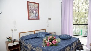 Un dormitorio con una cama, una mesita de noche, una lámpara de pared, un cuadro enmarcado y una ventana con cortinas.