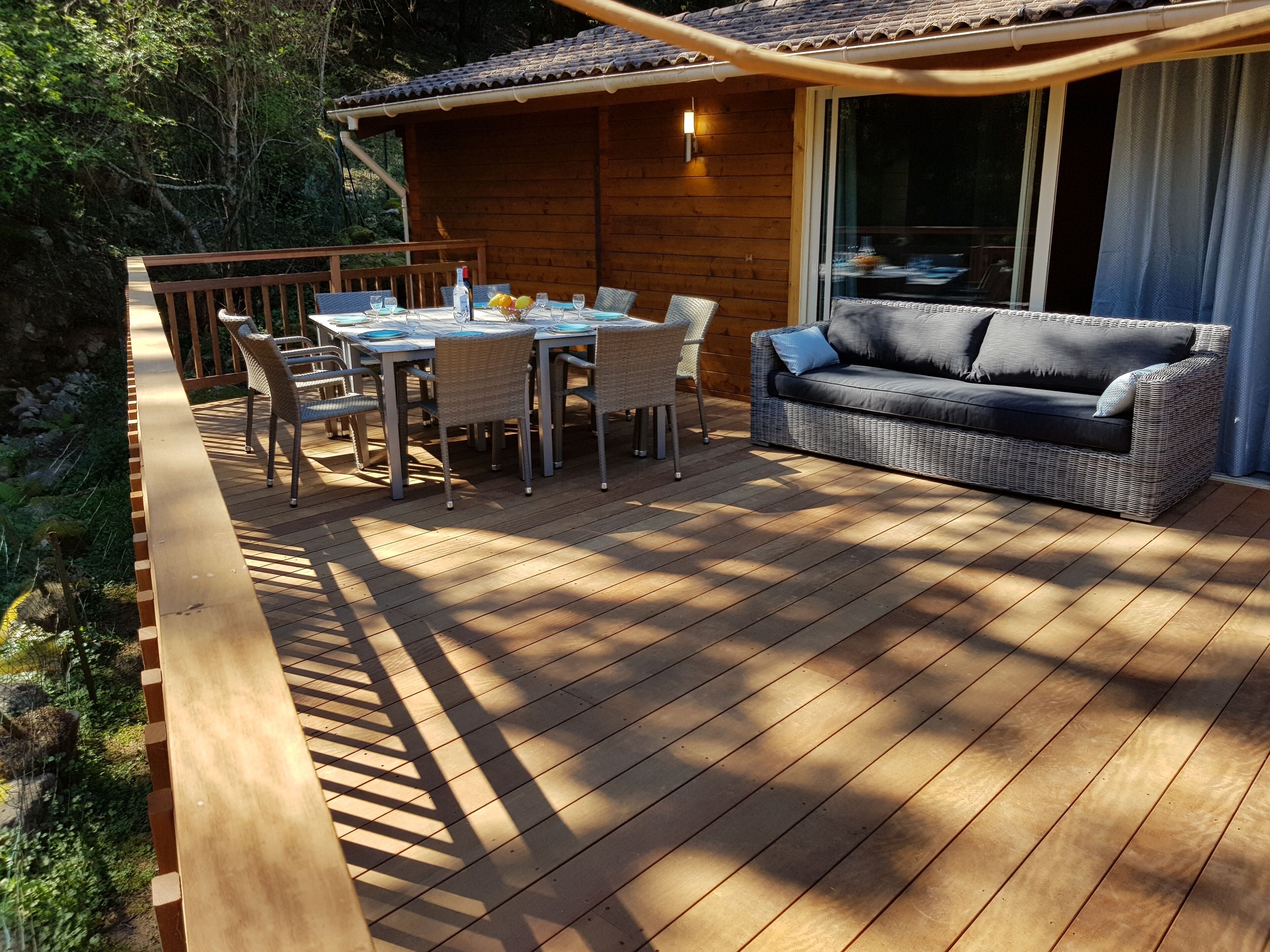A wooden deck with a table and chairs, a sofa, and a small wooden structure with a window.