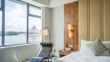 A hotel room with a large window, a massage chair, a wooden headboard, and a bed with patterned bedding.