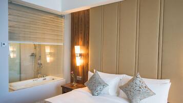 A hotel room with a large bed, a nightstand, a wall-mounted lamp, and a bathroom with a bathtub and shower.