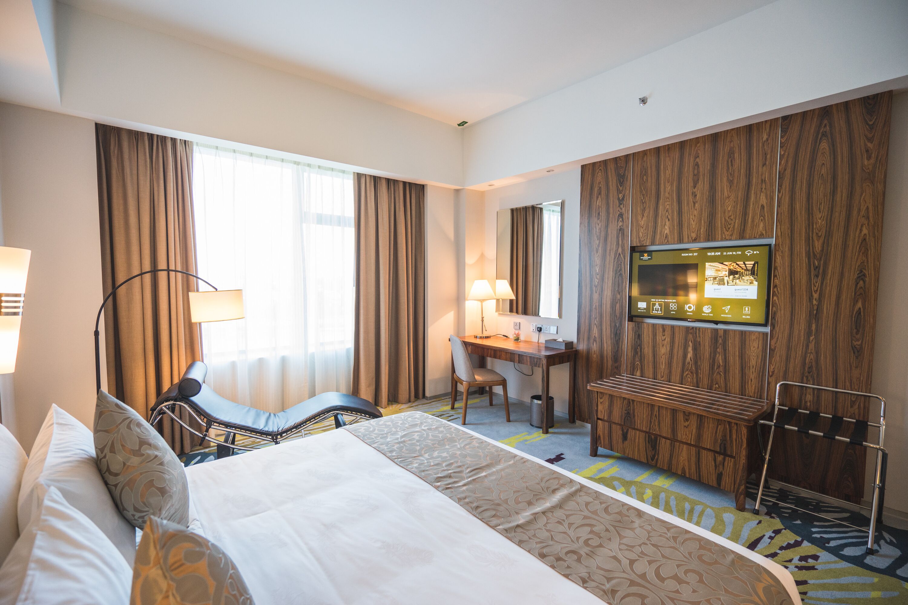 A hotel room with a bed, a desk, a chair, a TV, and a window with curtains.