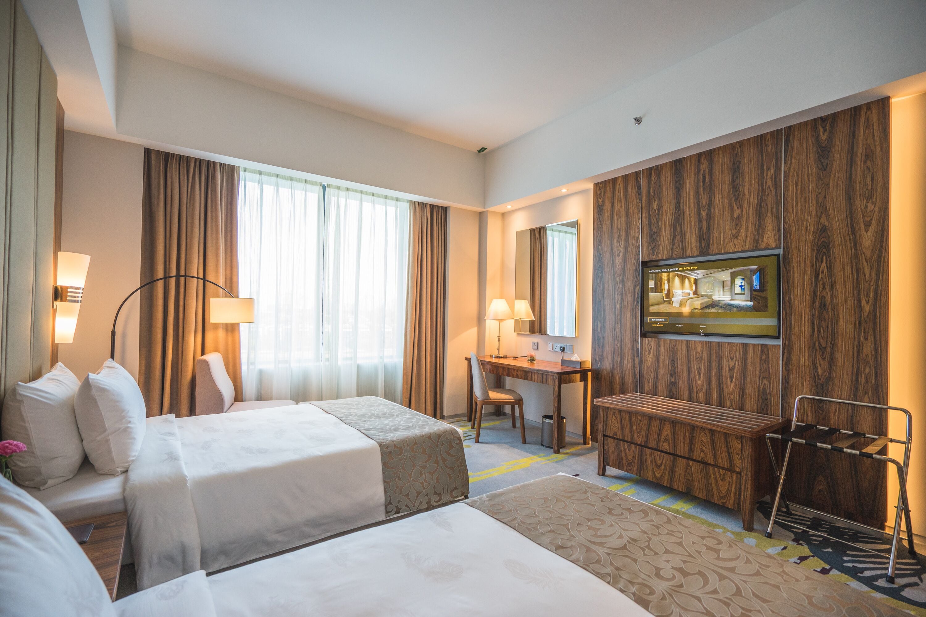 Habitació d'hotel amb dos llits, un escriptori, una cadira, un televisor i un bany.
